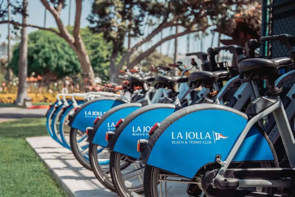 White bicycles with blue accents parked in a bike rack on a lawn at La Jolla Beach & Tennis Club