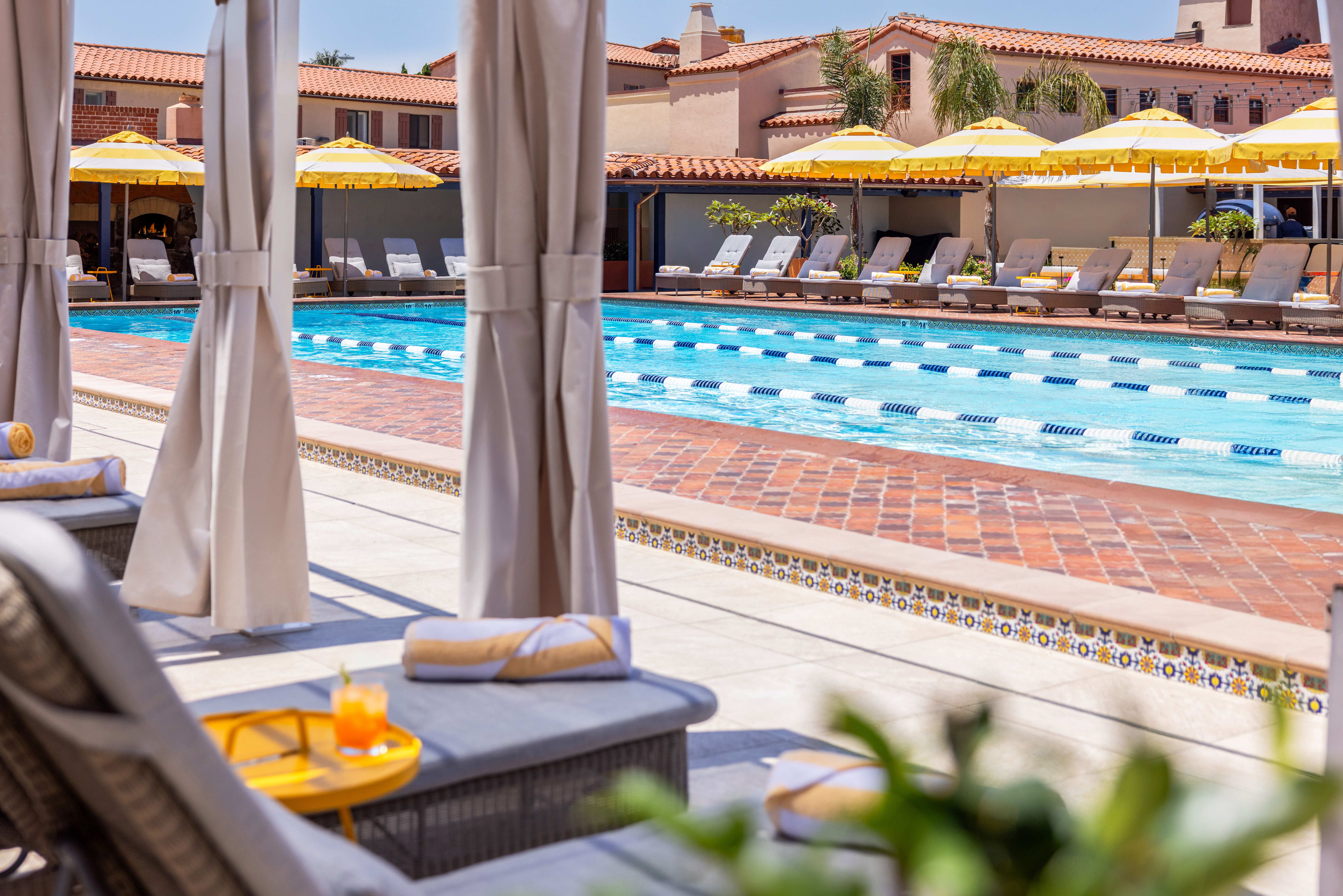 Pool deck with private cabanas and lounge chairs beneath yellow and white umbrellas